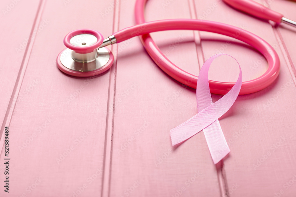 Fototapeta premium Pink ribbon with stethoscope on white wooden background. Breast cancer awareness concept