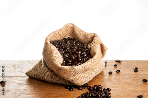 Roasted Coffee Beans spilled from Jute Bag on wooden boards with white background © SimoneO