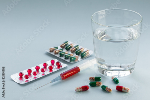 Tablets in blister pack, syringe with vaccine and glass of water on grey background.