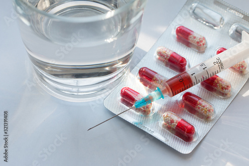 Tablets in blister pack, syringe with vaccine and glass of water on grey background.