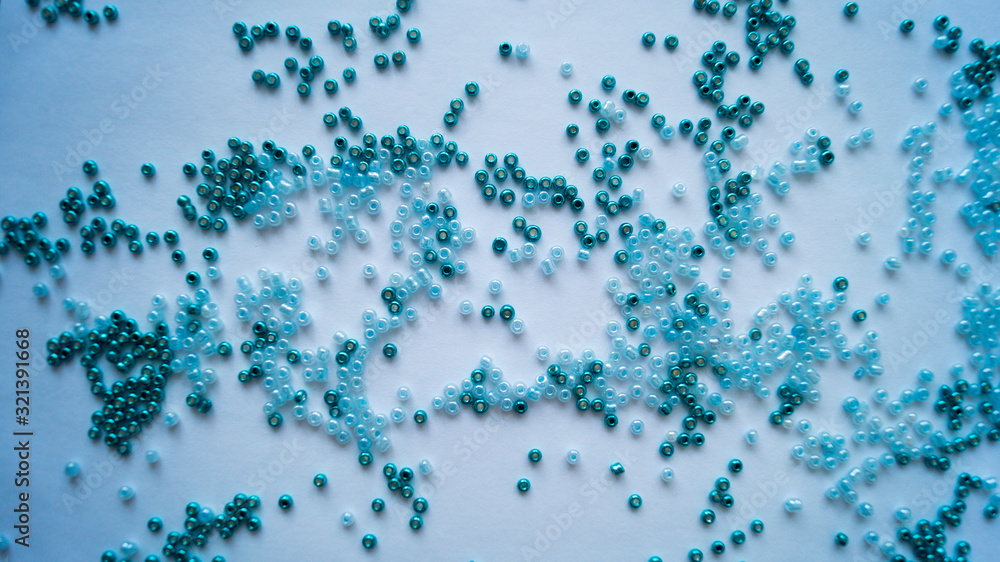 Blue-green beads scattered in a chaotic manner on a white background.