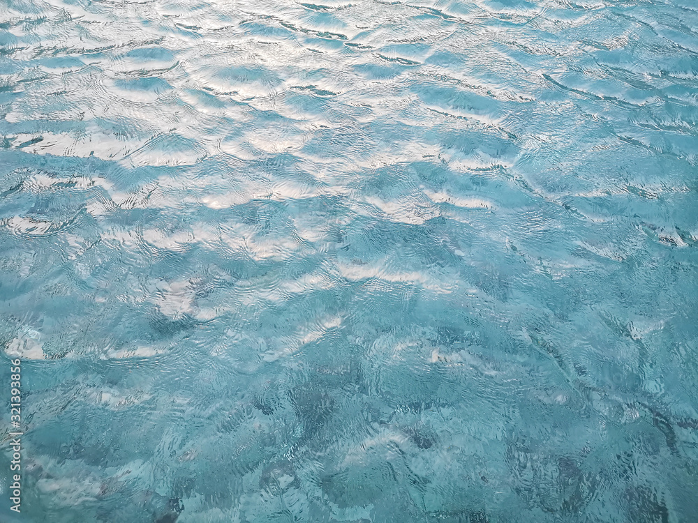 Obraz premium Waving pattern of vivid turquoise blue water in the swimming pool above stone tiles with soft light of reflection of the sunshine