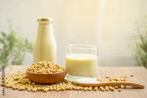 Fresh soybean seeds in brown wooden bowl, sugar in a spoon and two bottles of soy milk on the table, under sunlight morning blurred background, delicious healthy drinking for breakfast