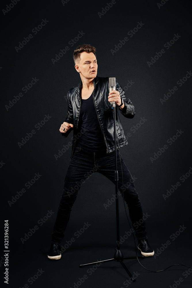 Man in black leather jacket , jeans and shirt with microphone in hand over dark background Man in black leather jacket , jeans and shirt with microphone in hand over dark background