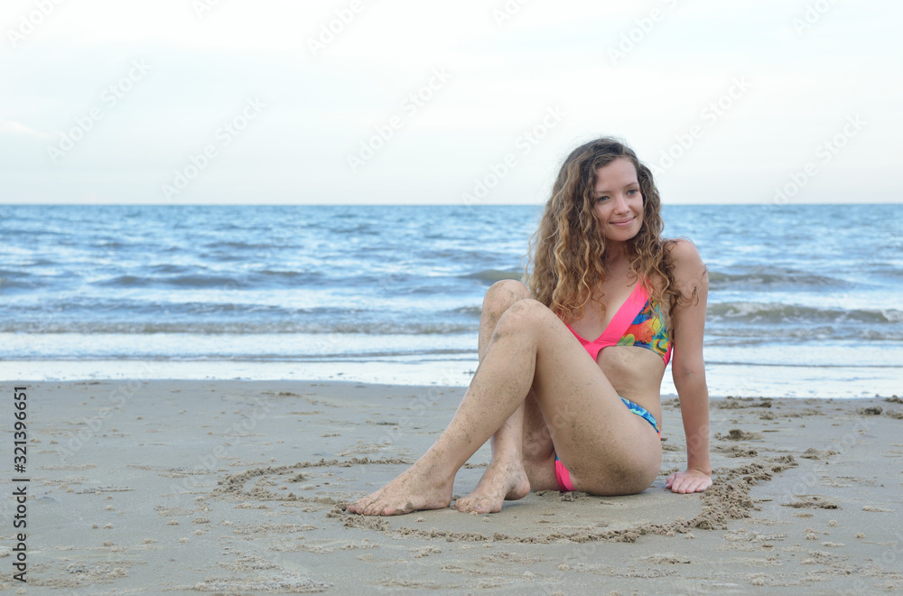 Pretty beautiful woman in pink bikini relaxing on the beach with heart love shape on the sand, Valentines and summer holiday concept Pretty beautiful woman in pink bikini relaxing on the beach with heart love shape on the sand, Valentines and summer holiday concept