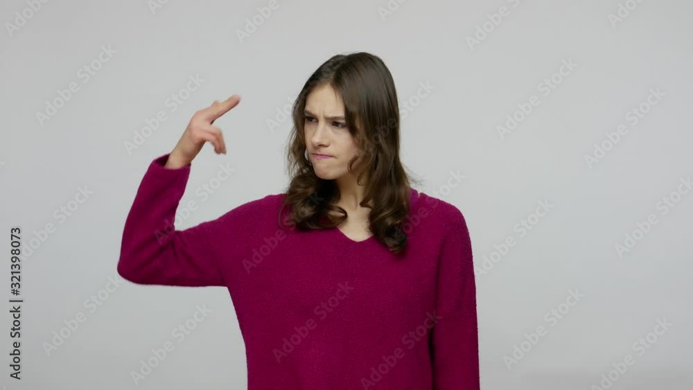 Depressed brunette woman looking at finger pistol with desperate helpless expression, performing suicide gesture, shooting with finger gun into head. indoor studio shot isolated on gray background Depressed brunette woman looking at finger pistol with desperate helpless expression, performing suicide gesture, shooting with finger gun into head. indoor studio shot isolated on gray background