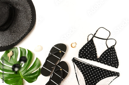 Woman's swimwear and beach accessories flat lay top view on white background. black and white polka dot bikini swimsuit, black straw hat, shoes, sunglasses, monstera leaf, shells. Copy space photo