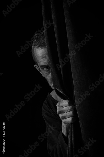 Scared man peeping from behind the curtain.