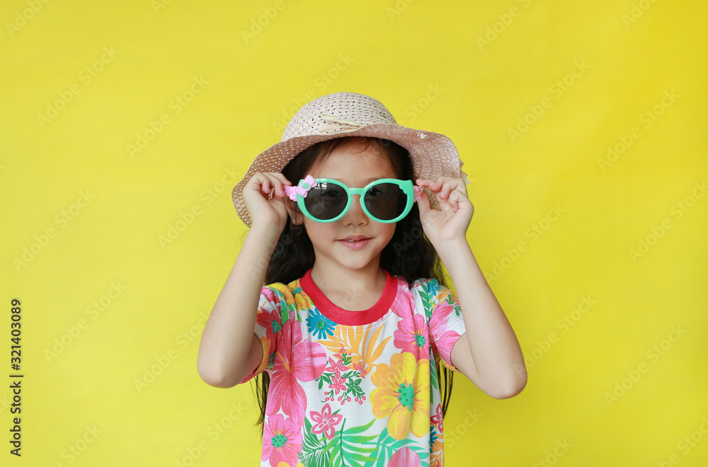 Portrait asian child girl in floral pattern summer dress and hat wearing a sunglasses on yellow background. Fahion of holiday and summer concept Portrait asian child girl in floral pattern summer dress and hat wearing a sunglasses on yellow background. Fahion of holiday and summer concept