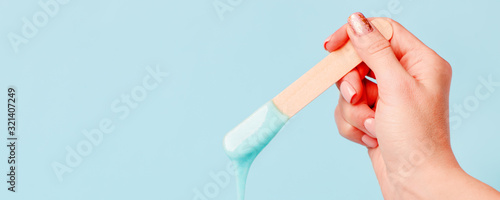 depilation and beauty concept - sugar paste or wax honey for hair removing with wooden waxing spatula sticks in hand on blue background, copy space, beauty industry, concept of smooth skin remove photo