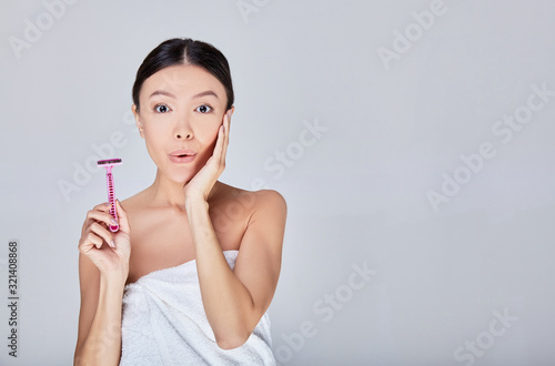 Surprised young Asian woman after shower with a pink razor in her hand.