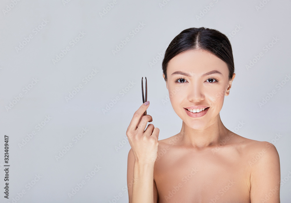 Asian woman holds tweezers in her hand and poses on a gray background. Asian woman holds tweezers in her hand and poses on a gray background.