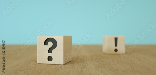 wooden cubes with black question mark foreground and exclamation mark sign in the background on wooden table