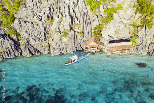 Fototapeta Naklejka Na Ścianę i Meble -  View from above, stunning aerial view of some bungalows surrounded by rocky cliffs bathed by a turquoise, crystal clear sea. Malwawey Coral Garden, Coron Island, Palawan, Philippines.