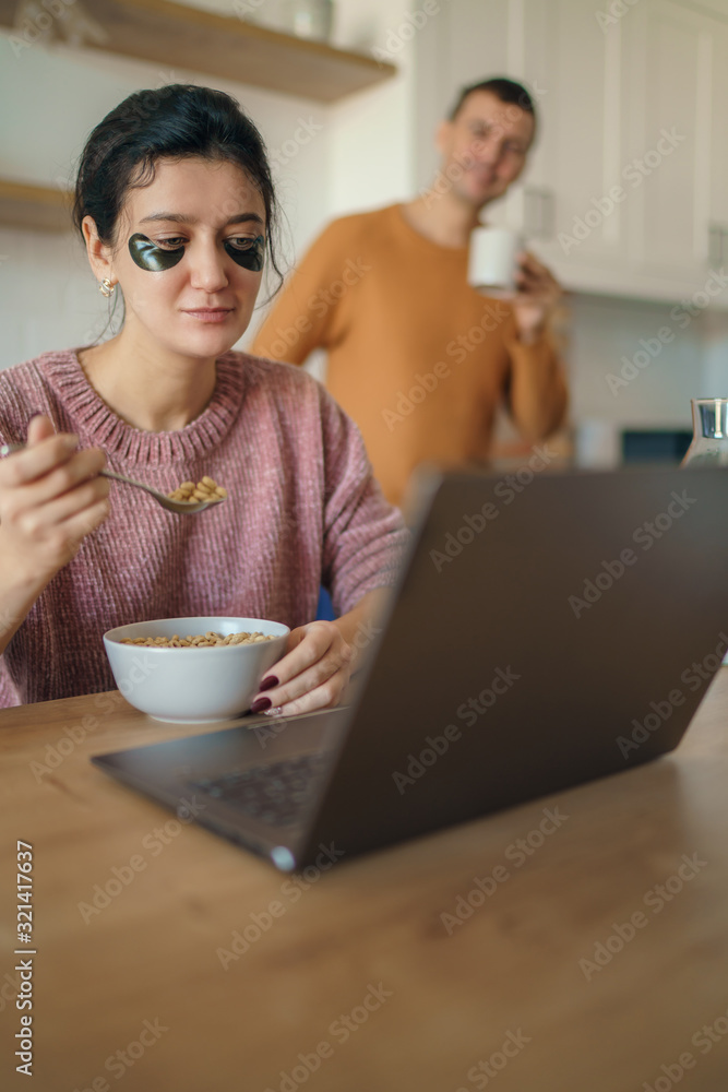 Beautiful young married couple having breakfast together working on laptop at table or reading news. Loving husband and wife making plans for vacation in the kitchen at home Beautiful young married couple having breakfast together working on laptop at table or reading news. Loving husband and wife making plans for vacation in the kitchen at home