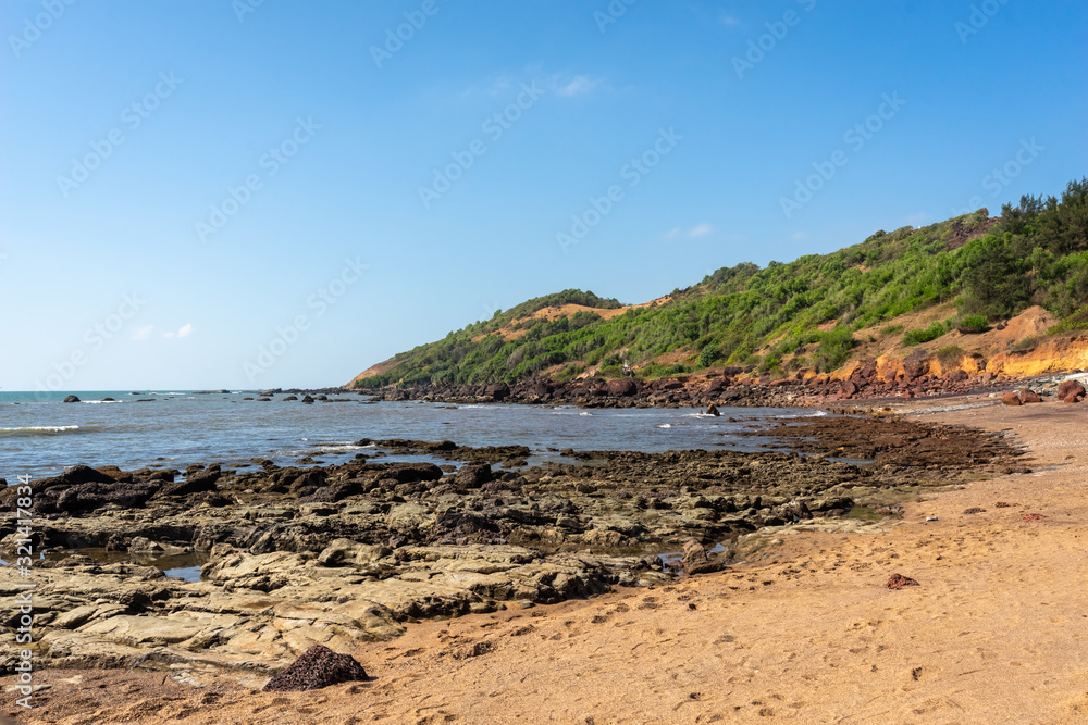 Anjuna beach, Goa state, India. Panoramic ocean view of beautiful tropical coast with green trees and mountains.