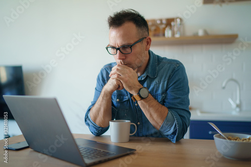 Thoughtful serious young man lost in thoughts in front of laptop, focused businessman thinking of problem solution, worried puzzled man looking ar laptop screen