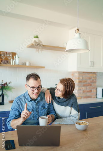 Beautiful young married couple having breakfast together working on laptop at table or reading news. Loving husband and wife making plans for vacation in the kitchen at home