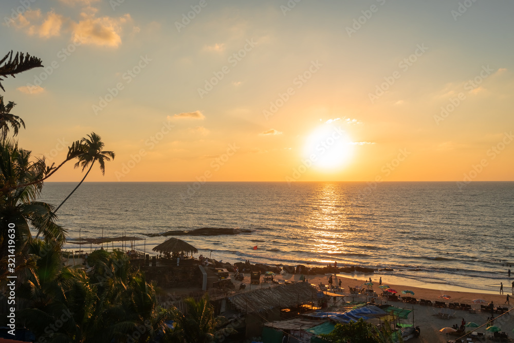 Sunset on the tropics. Amazing view of ocean coast with silhouettes of palms on setting sun background. Sand beach and horizon in pink and orange colors. Beautiful sunset sky. Sunset on the tropics. Amazing view of ocean coast with silhouettes of palms on setting sun background. Sand beach and horizon in pink and orange colors. Beautiful sunset sky.