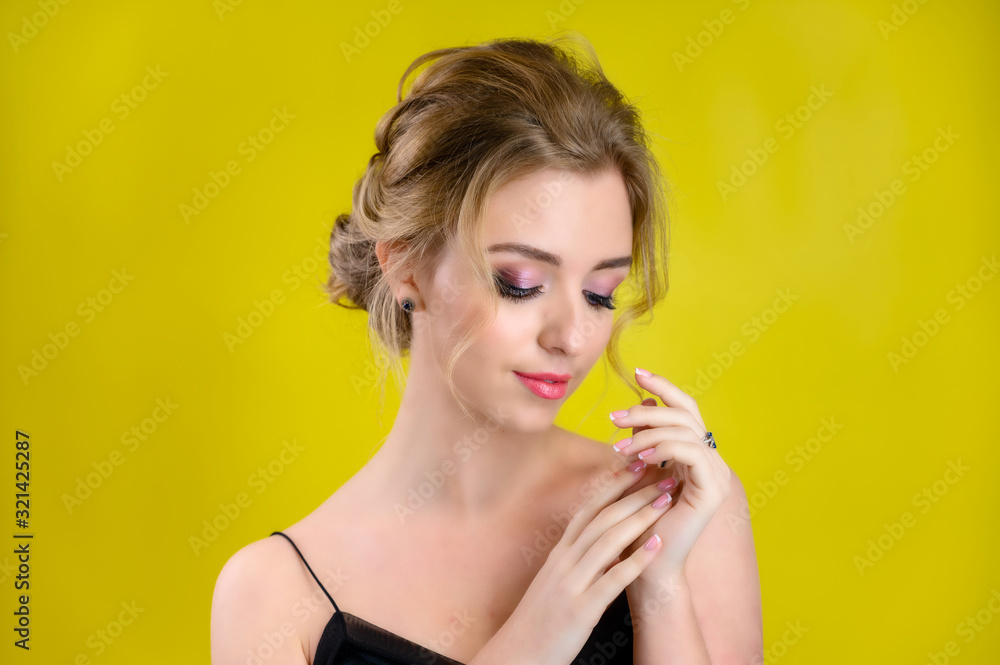 Naklejka premium The concept of cosmetics, fashion and style. Glamorous beauty portrait of a pretty blonde model with excellent makeup and a beautiful hairstyle on a yellow background in the studio.