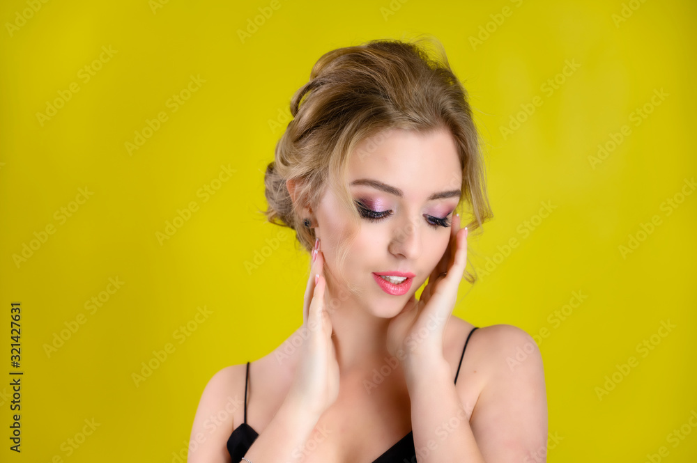 Glamorous beauty front view portrait of a pretty blonde model with excellent make-up and beautiful hairstyle on a yellow background in the studio. The concept of cosmetics, fashion and style. Glamorous beauty front view portrait of a pretty blonde model with excellent make-up and beautiful hairstyle on a yellow background in the studio. The concept of cosmetics, fashion and style.