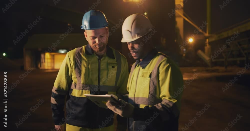 Concrete manufactory industry workers using tablet outside factory late at night Concrete manufactory industry workers using tablet outside factory late at night