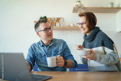 Beautiful young married couple having breakfast together working on laptop at table or reading news. Loving husband and wife making plans for vacation in the kitchen at home
