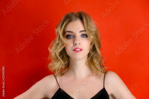 The concept of cosmetics, fashion and style. Glamorous beauty front view portrait of a pretty model with blond hair with great makeup and a beautiful hairstyle on a red background in the studio.