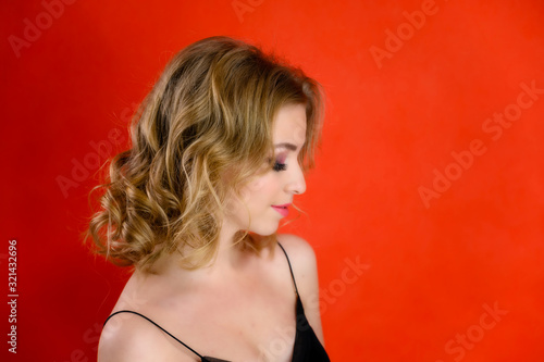Glamorous beauty portrait side view of a pretty model with blond hair with great makeup and a beautiful hairstyle on a red background in the studio. The concept of cosmetics, fashion and style. © Вячеслав Чичаев