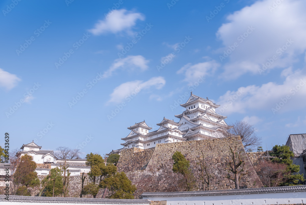 Himeji old defence stone wall with architectural castle complex on hill with floating white clouds casting shadows Himeji old defence stone wall with architectural castle complex on hill with floating white clouds casting shadows