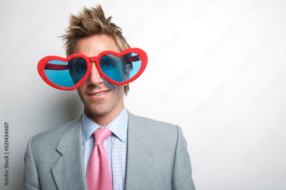Businessman with oversize red heart glasses smiling with wide eyes Businessman with oversize red heart glasses smiling with wide eyes