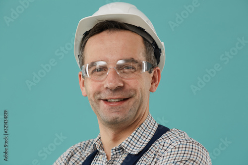Head and shoulders portrait of professional worker or builder smiling at camera while posing confidently against blue background, copy space photo