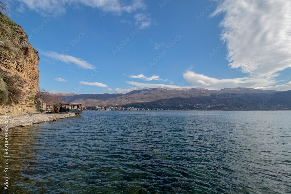 A series of lake landscapes. The crystal clear water against the backdrop of rock, mountain hills, and cloudy sky. Ohrid Lake, Northern Macedonia.