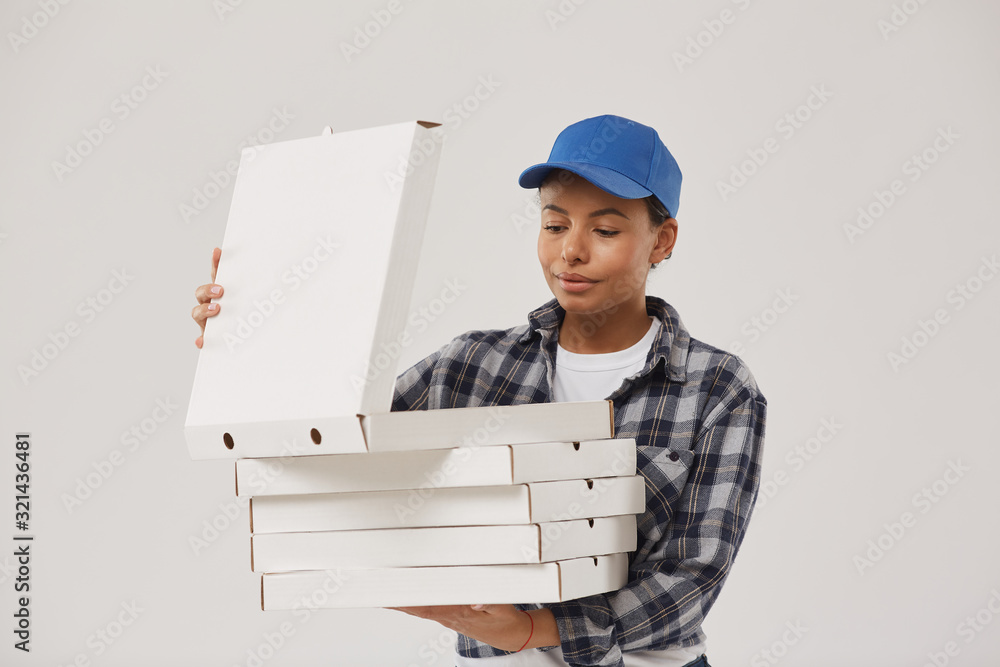 Waist up portrait of beautiful young woman holding pizza boxes and looking inside while working for fast food delivery and standing against white background, copy space Waist up portrait of beautiful young woman holding pizza boxes and looking inside while working for fast food delivery and standing against white background, copy space