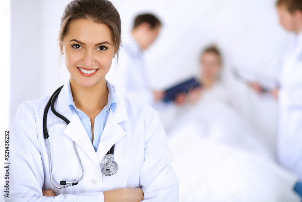 Female doctor smiling on the background with patient in the bed and two doctors