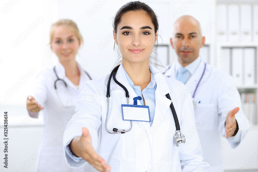 Doctor woman showing OK in clinic with colleagues at the background. Hispanic or latin american staff in medicine Doctor woman showing OK in clinic with colleagues at the background. Hispanic or latin american staff in medicine