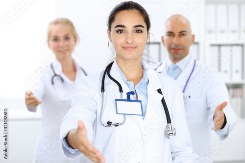 Doctor woman showing OK in clinic with colleagues at the background. Hispanic or latin american staff in medicine