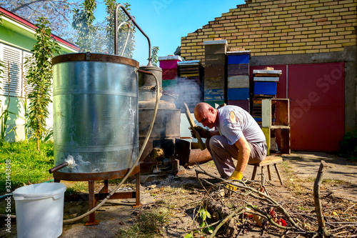 Billede på lærred Man is throwing firewood for maintaining fire under the distillation apparatus,