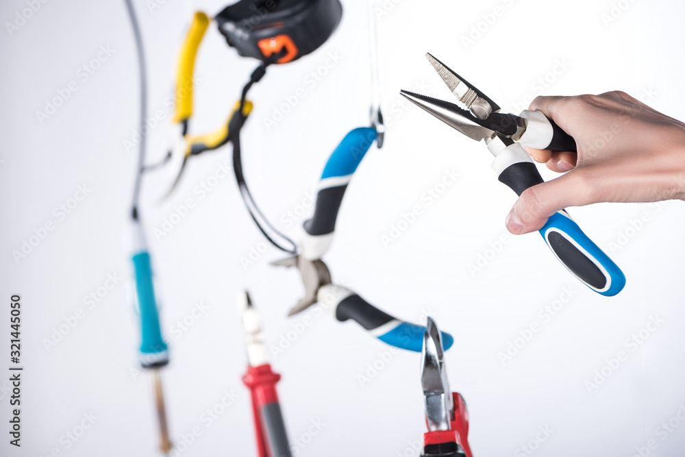 Cropped view of man holding pliers with levitating tools in air isolated on grey