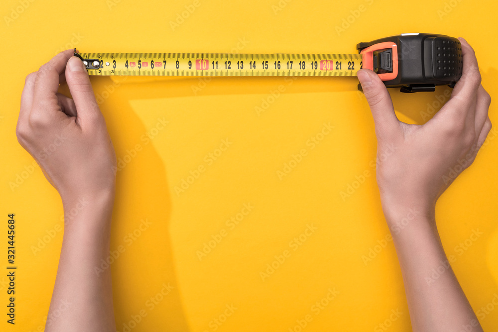 Top view of man holding industrial measuring tape on yellow background - obrazy, fototapety, plakaty 