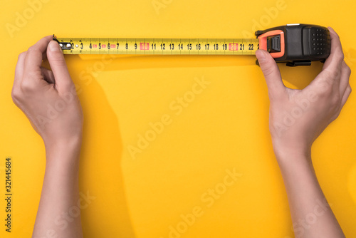 Top view of man holding industrial measuring tape on yellow background photo