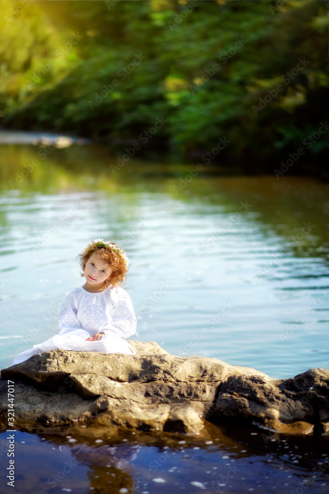 Vertical portrait of 5 years old girl in white traditional embroidery ukrainian dress and chamomiles wreath on rocks in river in Carpathian mountains. Travel tourism destination in Ukraine. Vertical portrait of 5 years old girl in white traditional embroidery ukrainian dress and chamomiles wreath on rocks in river in Carpathian mountains. Travel tourism destination in Ukraine.