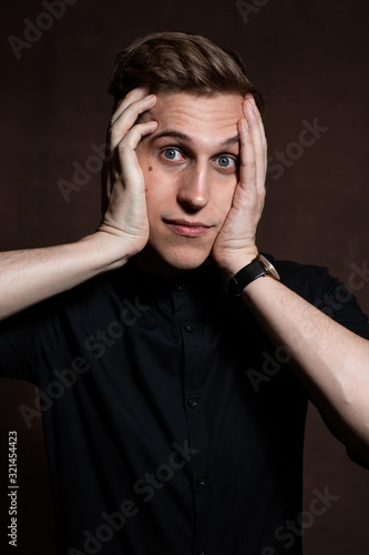 A man in round glasses and a black shirt is grimacing