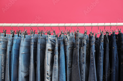 Rack with stylish jeans on pink background, closeup