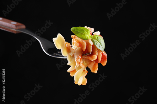 Delicious fusilli pasta with tomato sauce on fork against black background