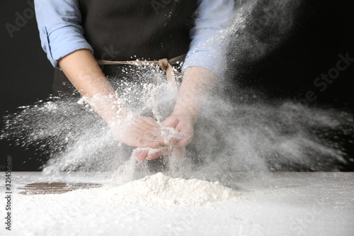 Woman working with flour at table against black background, closeup