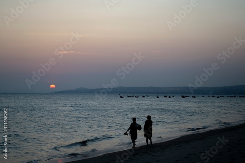 Beautiful sunset on the beach with women and boats silhouettes.