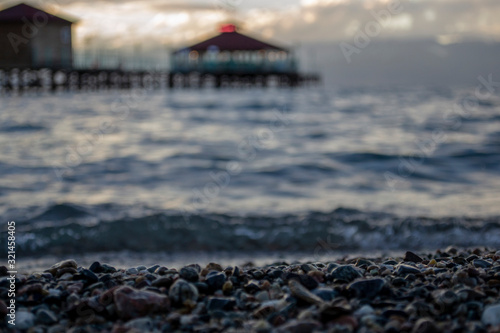Pebble beach with unfocused lake and pier background.