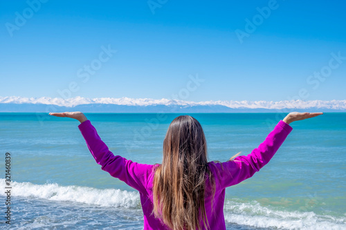 Young woman standing on the coast of mountain lake and holding mountains on her hands.