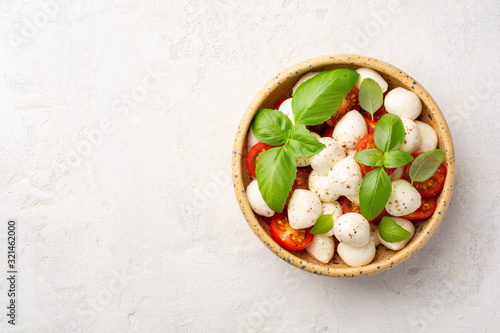 Traditional Italian caprese salad with mozzarella cheese, cherry tomatoes and basil in ceramic bowl on concrete background. Top view, copy space.
